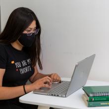Estudiante sentada en escritorio, escribiendo en computadora