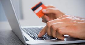 Persona frente a computadora con tarjeta bancaria en mano